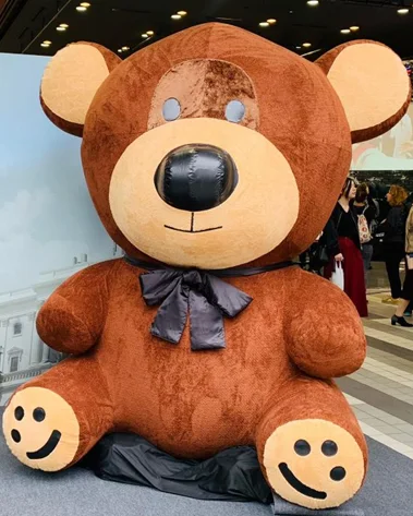 The finished giant bear installed indoors at the event, seated with its bow on, people passing behind it