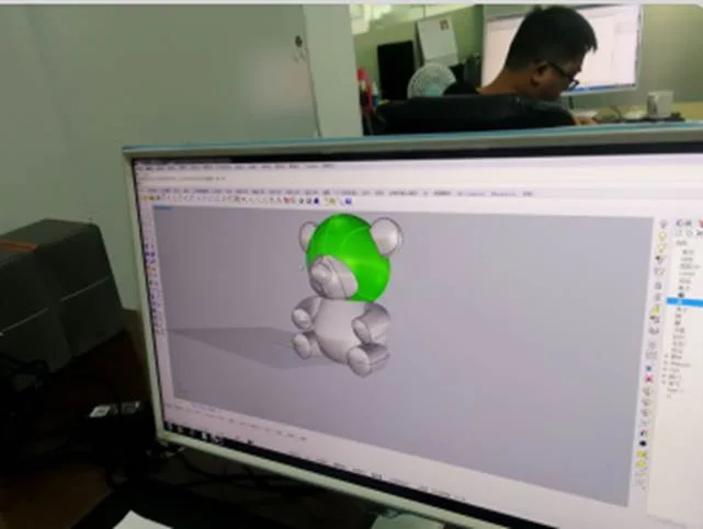 A designer at a workstation, the bear model on screen with one part highlighted for editing
