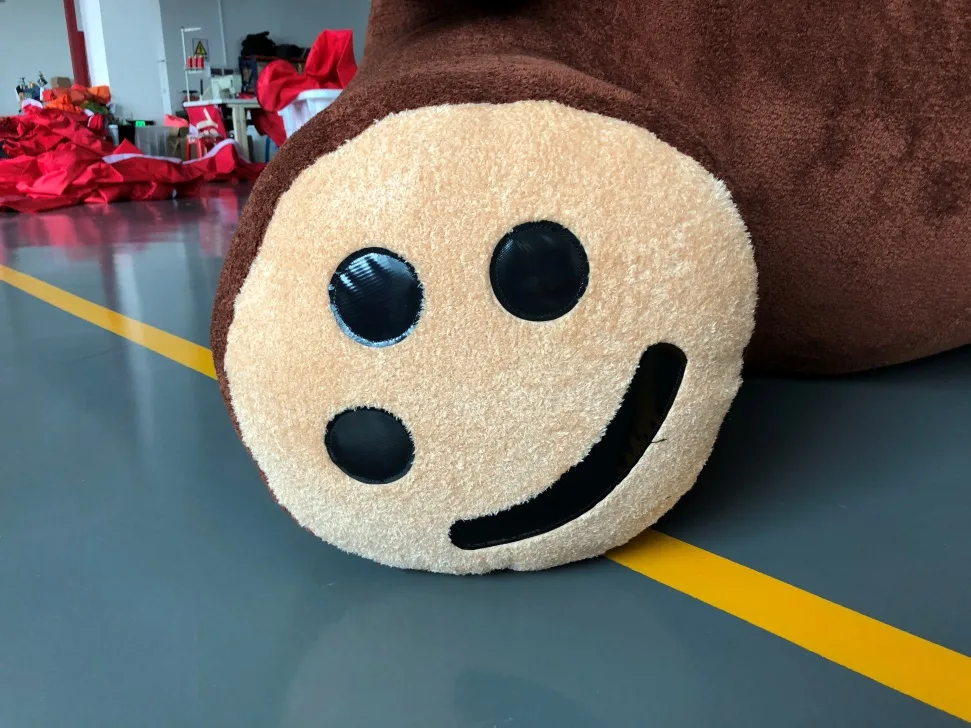 Close-up of one plush paw, cream pad with black appliqué toe and heel pads, against the factory floor