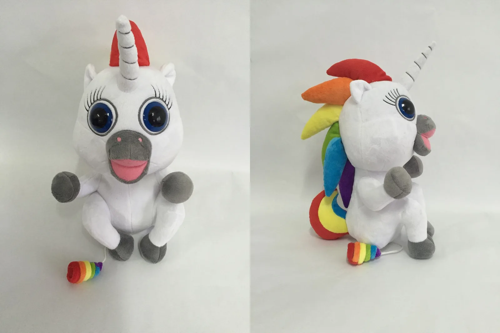 The revised unicorn sample from the front and the side: white plush, big blue eyes with embroidered lashes, grey muzzle with an open pink mouth, a six-colour mane, and a rainbow soft-serve on a cord at its feet